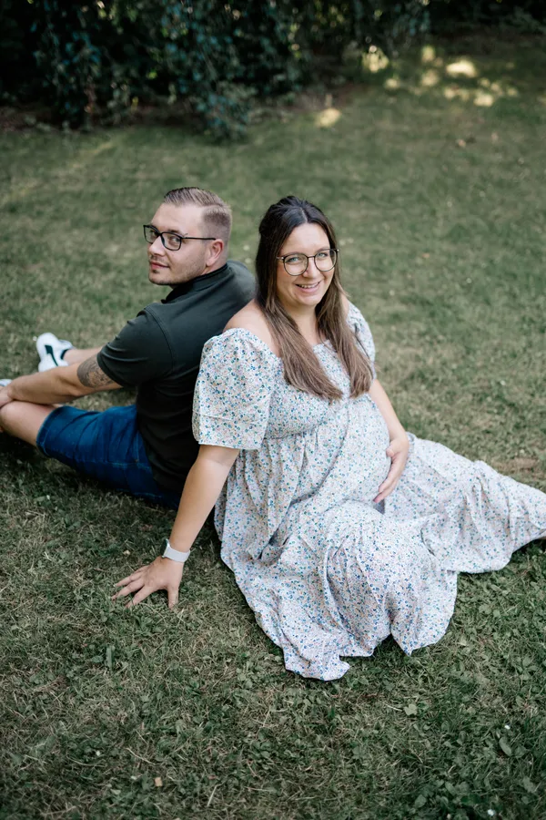 Paar mit Babybauch sitzt im Gras