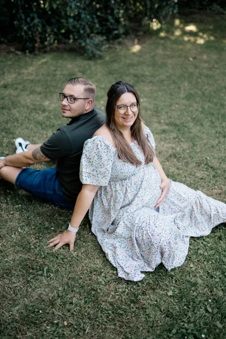 Paar mit Babybauch sitzt im Gras